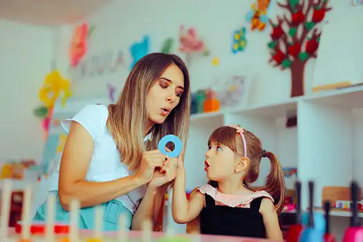 Kvinnelig logoped og en liten jente trener på lyden O. Logopeden holder en lysblå O